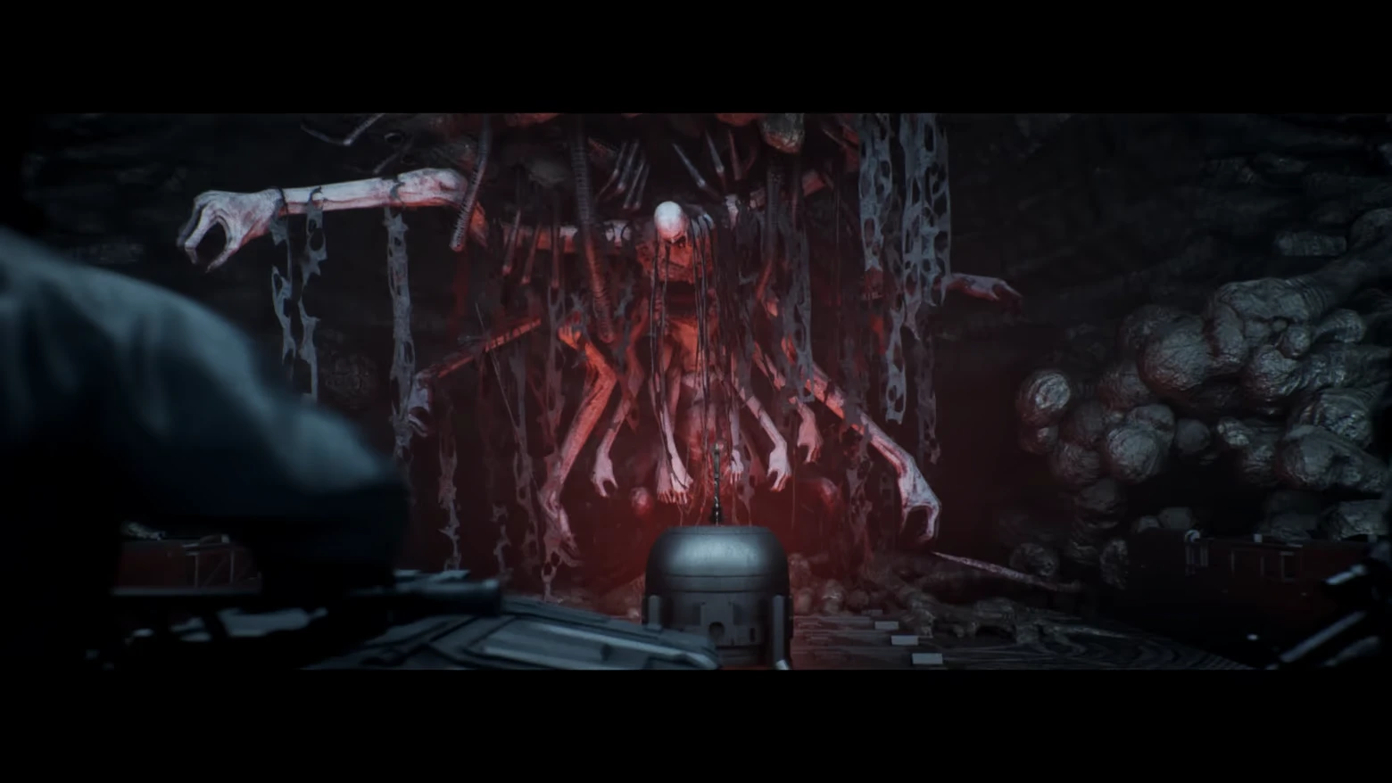 Flesh Cocoon Horror – AINUR AINUR: Red-lit humanoid mass with many arms hanging in a dark rocky cave chamber.