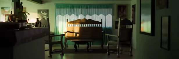 Animas Prologue: A dimly lit room with wooden chairs, a bench, green curtains, and framed pictures.