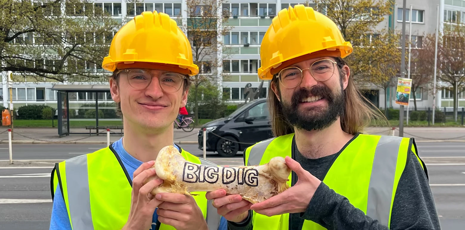 Big Dig: Two workers in yellow hard hats hold a bone labeled “BIG DIG”.