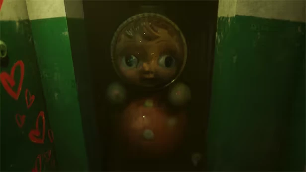 MATRESHKA: A large doll with wide eyes in a dim hallway, red hearts painted on green walls.