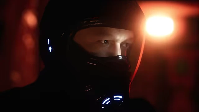 Project Vesperi: A person in a dark helmet with glowing blue lights, illuminated by a red-orange glow.