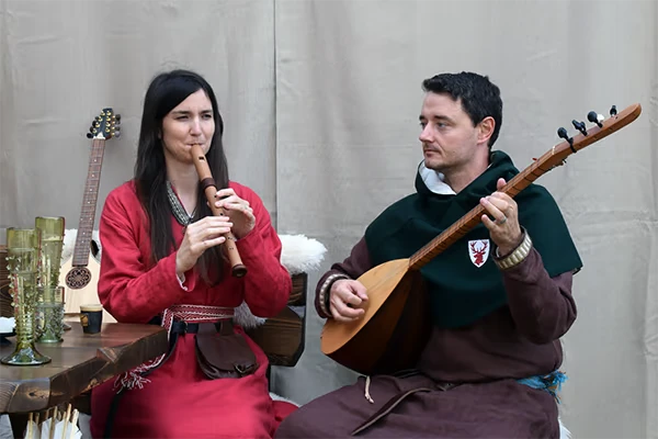 Scarlet Deer Inn: Two musicians in medieval attire play a flute and lute beside a wooden table.