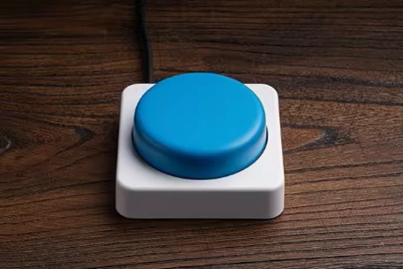 Button Closeup – SPiNG SPiNG: Large blue button on a white base, placed on a wooden surface.